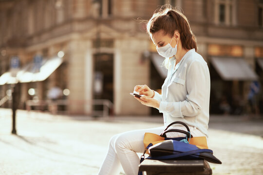 young woman wiping smartphone with sanitizer outdoors in city