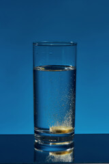 Close up of glass of water with effervescent aspirin tablet, pill in it isolated over blue background. Health concept