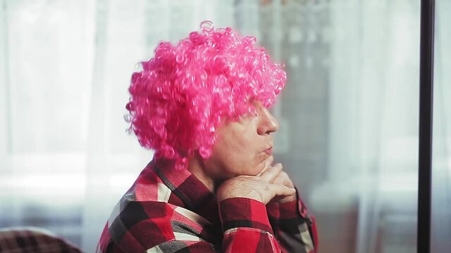 A man in front of a mirror puts on a clown wig with pink curls.