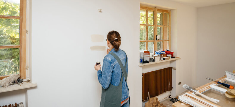 Rear view of a curious woman during the renovation of house apartment testing multiple colors on the white wall - warm clam tones