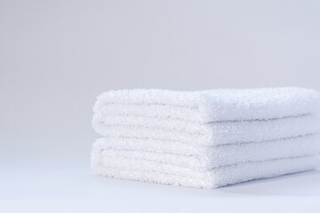 View of a stack of white folded terry towels on a light background.