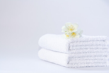 Fototapeta na wymiar Two white neatly folded terry towels with a jasmine flower on a light background.