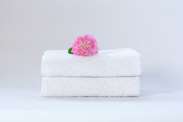 Two white neatly folded terry towels with a rose flower on a light background.