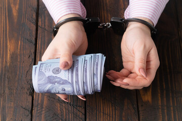 female hands in handcuffs hold twisted money on a dark wooden background
