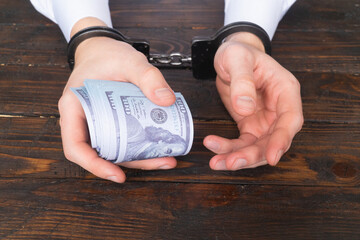 male hands in handcuffs hold twisted money on a dark wooden background