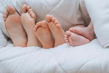 Legs of a family covered with a plaid closeup. Mom, daughter and newborn son are lying, sleeping under a white blanket. Photography, concept.