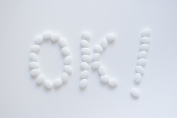 Motivational inscription OK with an exclamation mark made of white oval pharmaceutical tablets on a white sheet of paper background