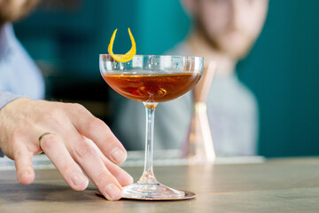Bartender presents a ready-made cognac-colored cocktail with lemon zest. Making a cocktail. Mixology