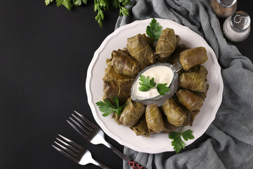 Dolma - stuffed grape leaves with rice and meat on white plate on black background. Traditional Caucasian, Greek, Ottoman and Turkish cuisine