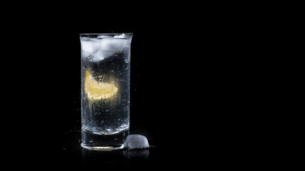 Refreshing full glass of water with a lemon slice and ice cubes isolated on black background