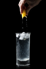 Squeezing a lemon into a clear glass of water isolated on black background. Fresh water in a glass with ice