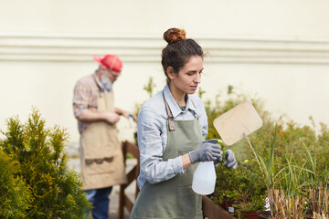 Waist up portrait of young woman caring for plants while working in outdoor garden or plantation, copy space © Seventyfour