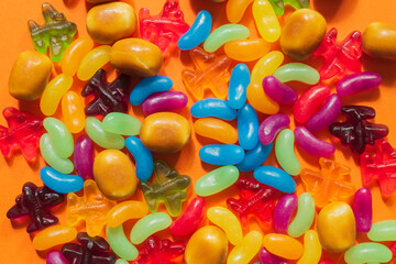 Multi-colored glazed jelly beans sweets on orange paper background