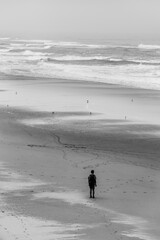 Person walking on the beach black and white portrait. Alone on a quiet isolated sandy beach. Hiking and exercise healthy lifestyle. Isolation and lonely state of mind concept