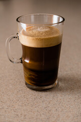 Morning fresh cup of coffee with swirling cream and crema layer in a glass mug