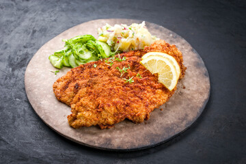 Traditionelles friettiertes Wiener Schnitzel mit Kartoffel und Gurken Salat angegeboten als close-up auf einem rustikalen Modern Design Teller mit Textfreiraum