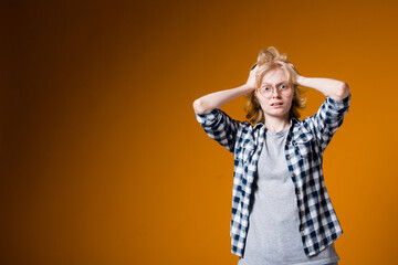 Upset blonde girl holding her head with his hands. Intense girl on an orange background looking at the camera.