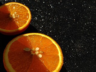 Orange is bright juicy on a black shiny background. Place for the buyer's text. A clear shadow passing through the middle of the orange slices.