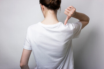 A girl in a T-shirt stands and points a hand to the back against a neutral background. Blank for...
