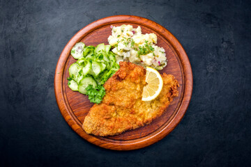Traditional deep-fried schnitzel with potato and cucumber salad offered as top view on a rustic...