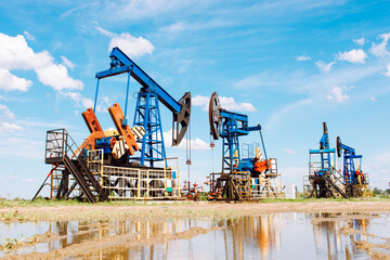 Fototapeta na wymiar Oil and gas industry. Working oil pump jack on a oil field with reflection on a puddle. White clouds and blue sky. Oil production