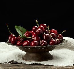 red ripe sweet cherries in a metal vintage bowl on a black background