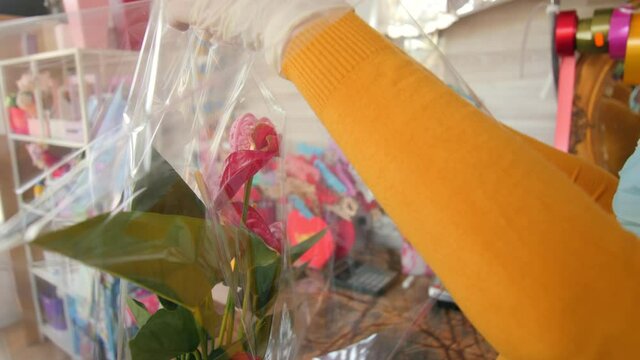 florist in gloves wraps potted calla plant with foil in shop