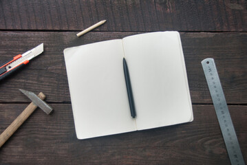 Building tools and opened notebook on dark wooden board. Copy space, flat lay
