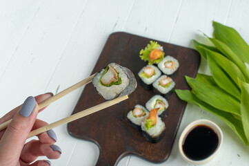 Female hand with chopsticks holds sushi roll. Sushi roll set with fried shrimp and salad