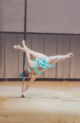 Girl in blue costume on pole dance championship showing acrobatic tricks. Pylon with little young...