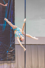 Picture of girl in light blue costume is showing acrobatic ticks on pylon. Little girl on championship on pole dance art. Straight legs above the head, as activity during quarantine.