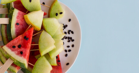 Fresh,ripe watermelon and melon sliced in white plate with watermelon seeds, wooden sticks and large copy space