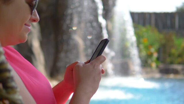Woman using phone by the waterfall on the vacations in 4k slow motion 60fps