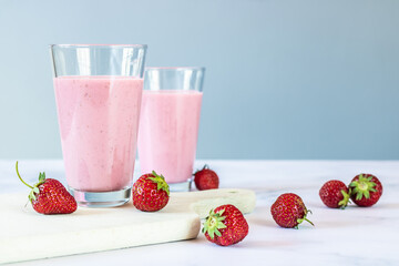 Strawberry milkshake on a chopping board with strawberries in the background