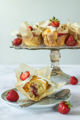 Vanilla muffins with strawberries and cherries, decorated with white chocolate coating (in the background more muffins and strawberries)