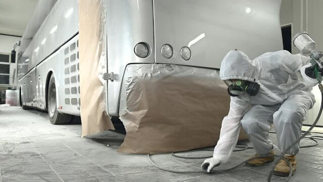 Bodyshop Worker In Full Protective Gear Checking New Spray Painting Job On Large Commercial Bus. 