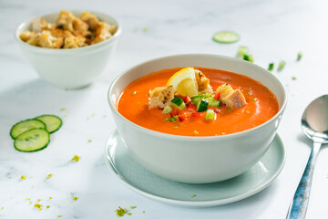 Gazpacho decorated with fresh vegetables (cucumber and pepper) with a bowl of toast in the background