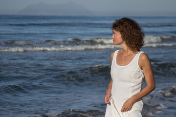 Fototapeta na wymiar Woman in white dress walking near a beach in sunny summer day, clear sky