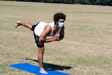 Man practising yoga in a field with face covering. Covid19