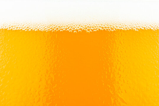Macro shot of beer in a glass with visible foam and water drops.