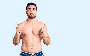 Fototapeta premium Young handsome man wearing swimwear pointing up looking sad and upset, indicating direction with fingers, unhappy and depressed.