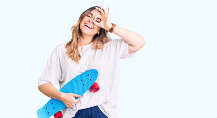 Young caucasian woman holding skate smiling happy doing ok sign with hand on eye looking through fingers