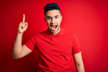 Fototapeta premium Young handsome man wearing red casual polo standing over isolated background pointing finger up with successful idea. Exited and happy. Number one.