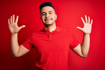 Naklejka premium Young handsome man wearing red casual polo standing over isolated background showing and pointing up with fingers number ten while smiling confident and happy.