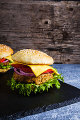 Two Fresh delicious homemade veggie burger lies on natural slate on rustic wooden background. Delicious tasty burger with lettuce, cheese, onion and tomato. buckwheat and lentil cutlet