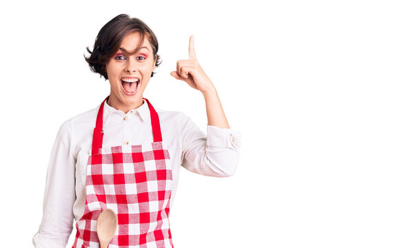 Beautiful young woman with short hair wearing professional cook apron pointing finger up with successful idea. exited and happy. number one.