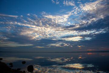 An abstract image taken at a lakefront at sunset. Image shows a spectacular cloudy sky and its reflection over water. Sky and water are separated only by a thin line of coast on the horizon. 