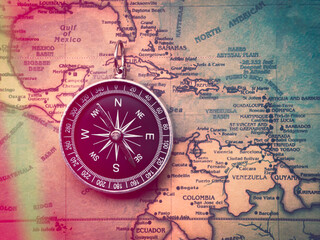 The compass is placed on the ancient or vintage world map between the United States of America and South America. Travel geography navigation concept background.