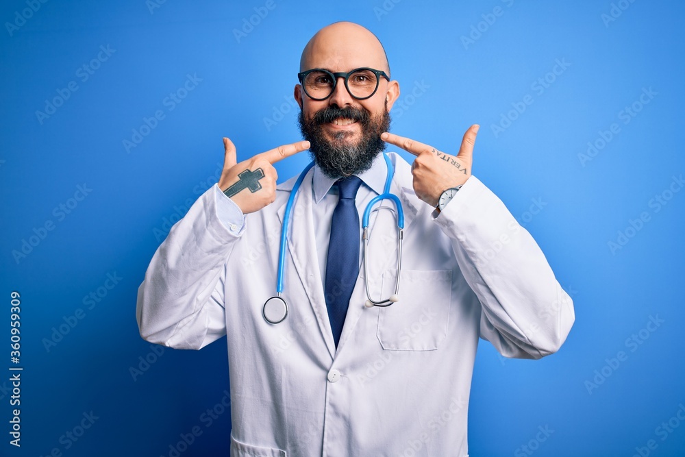 Poster handsome bald doctor man with beard wearing glasses and stethoscope over blue background smiling che