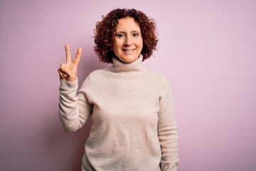 Middle age beautiful curly hair woman wearing casual turtleneck sweater over pink background...